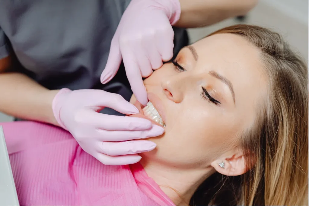 Dentist with pink gloves examining female patient's teeth and gums during post-extraction checkup